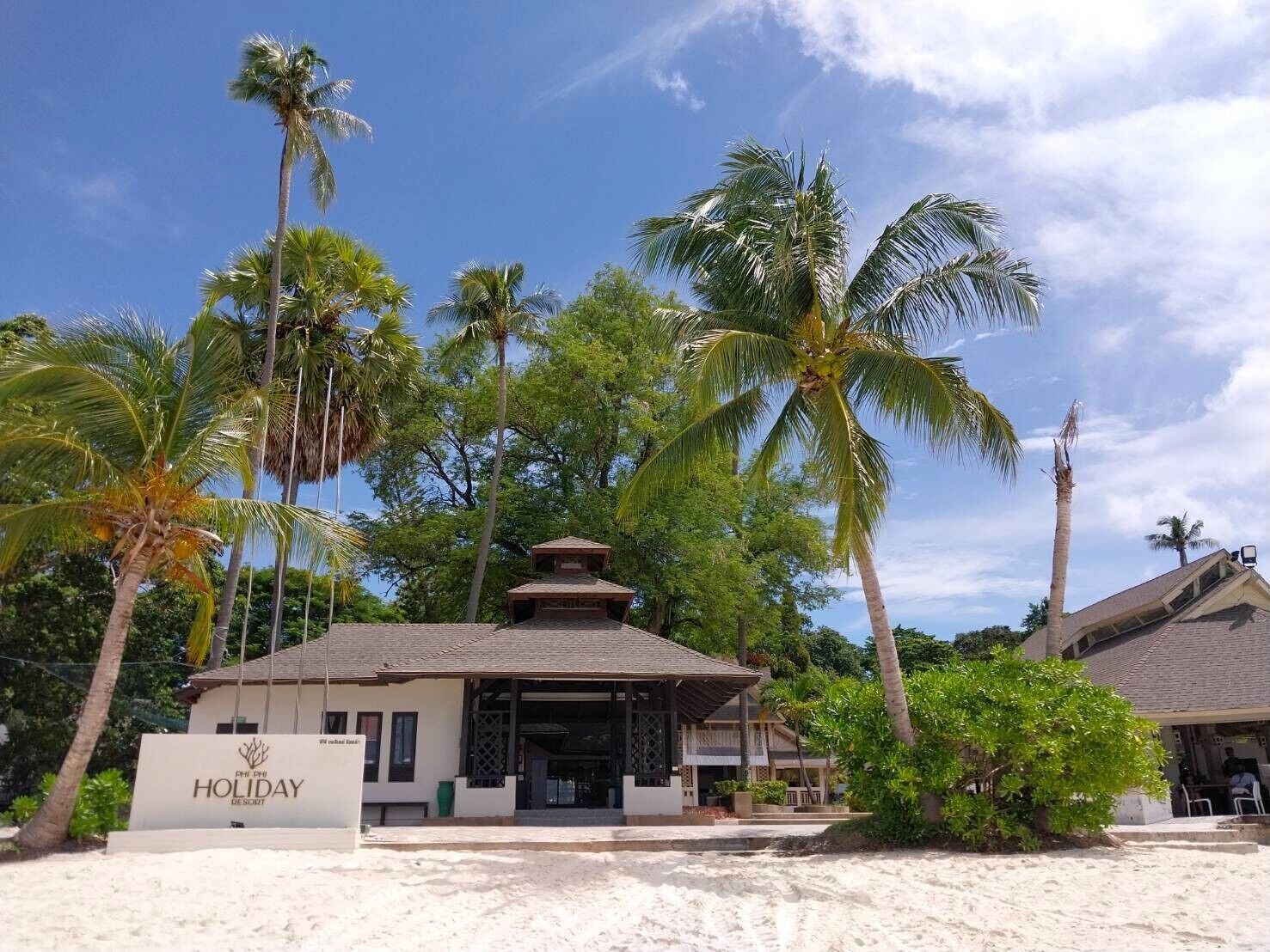 A resort with a sign reading 'Holiday Resort,' surrounded by palm trees and a sandy beach.