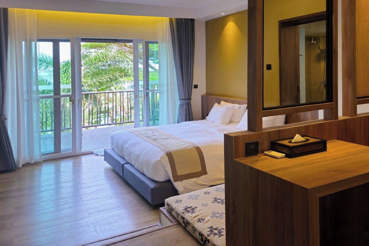 Une chambre d’hôtel comprenant un lit, une table de chevet, un miroir et une vue sur l’extérieur grâce à une porte-fenêtre coulissante.