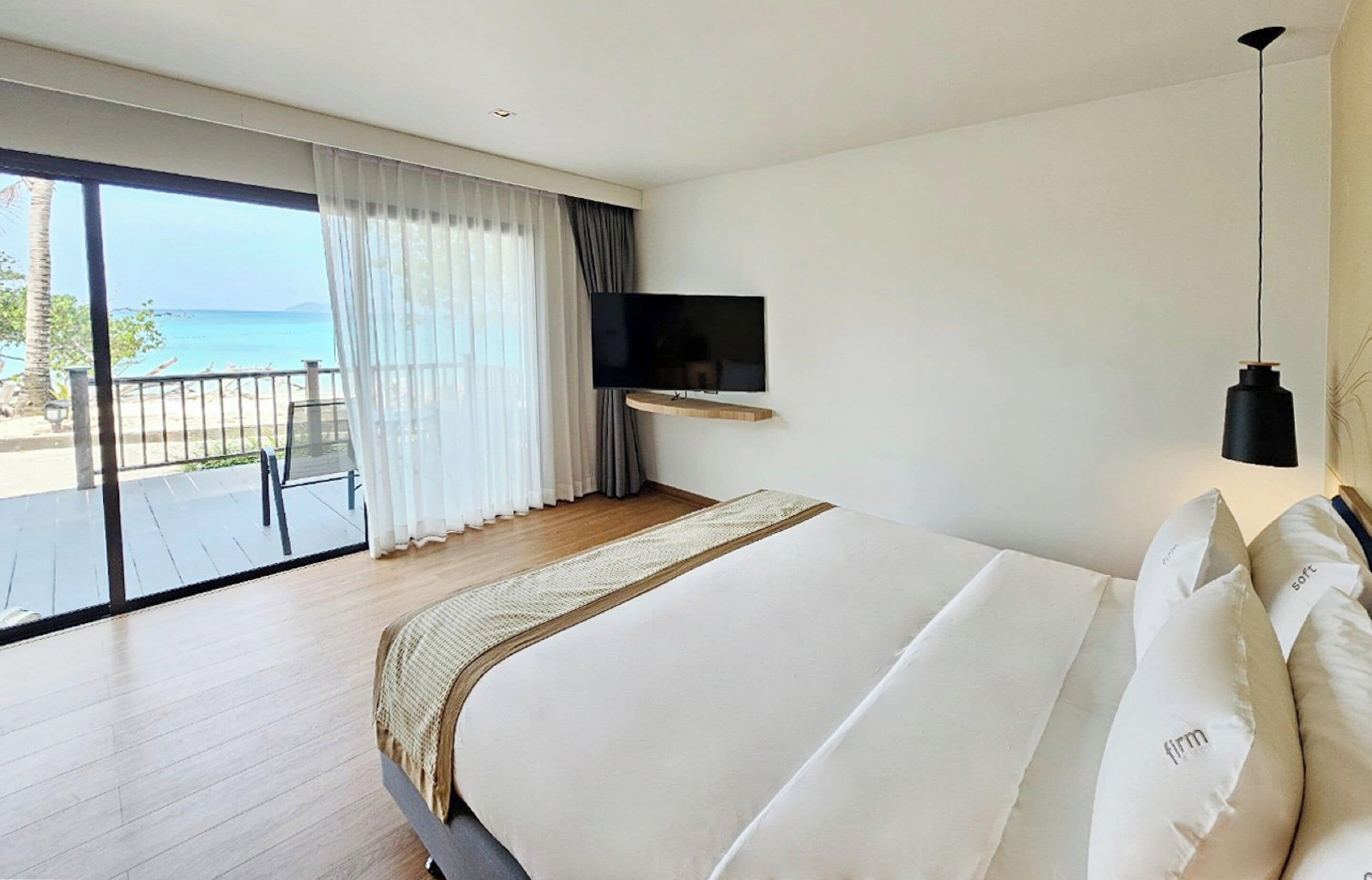 Habitación de hotel con una cama grande, televisión montada en la pared y un balcón con vistas al mar.