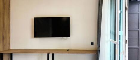 A room with a mounted TV on the wall, a wooden bench, and a window with a view.