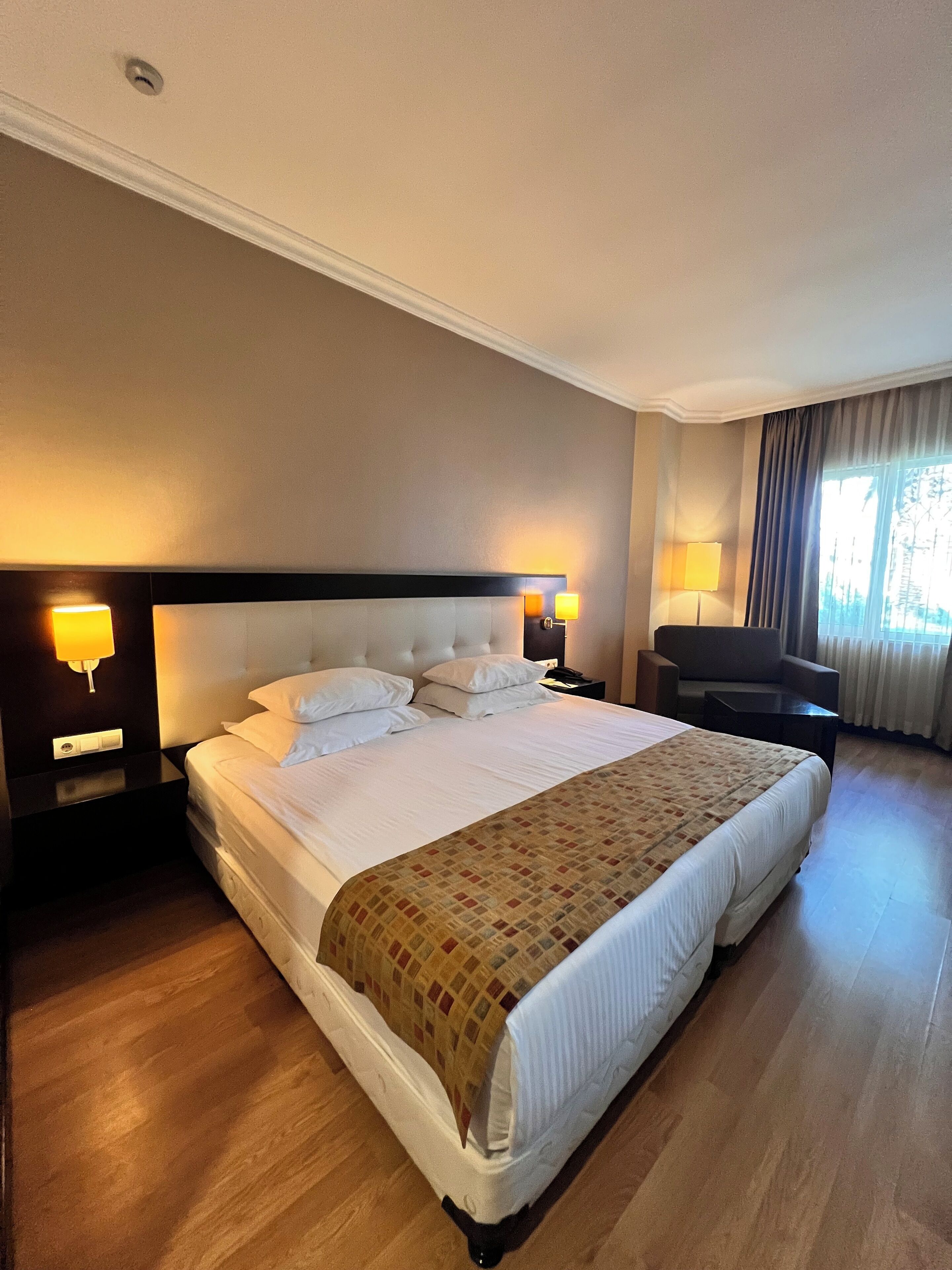 A hotel room with a large bed, two bedside tables with lamps, a chair, and a window with curtains.