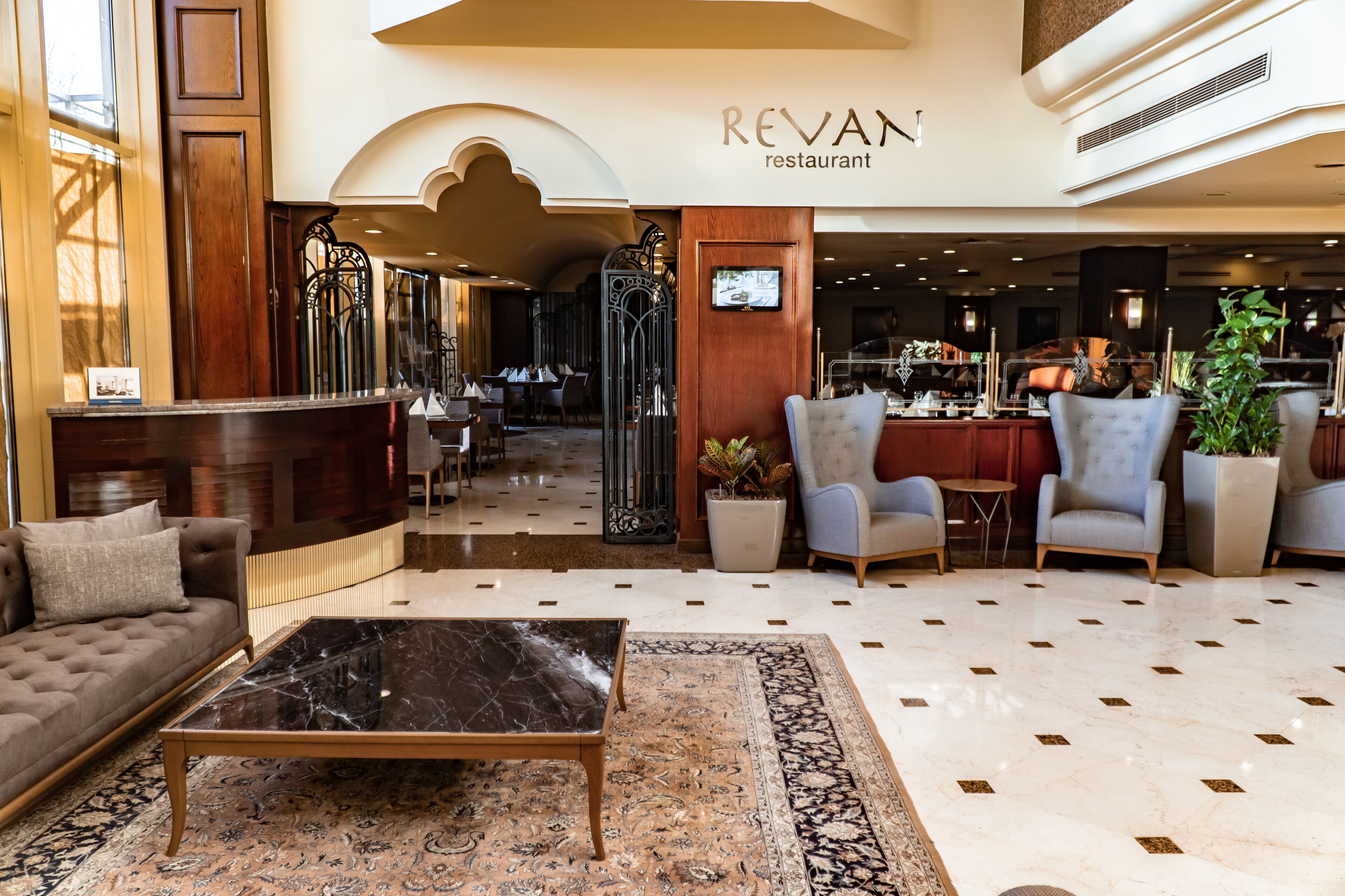 A spacious lobby with a reception desk, seating area, and a restaurant in the background.