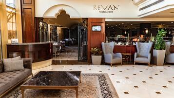 A spacious lobby with a reception desk, seating area, and a restaurant in the background.