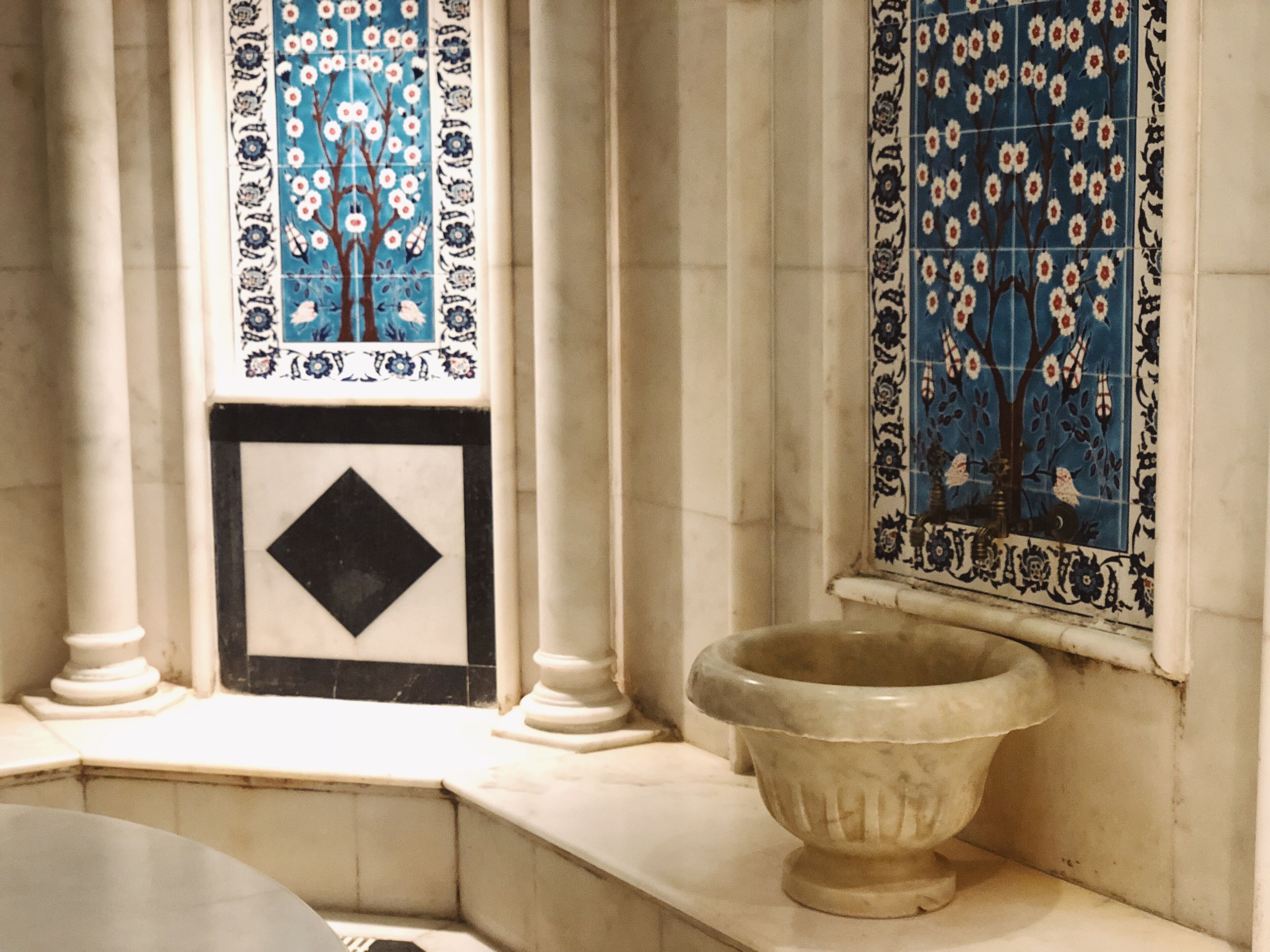 Un baño con lavamanos de mármol, azulejos decorativos y un cuadro enmarcado.