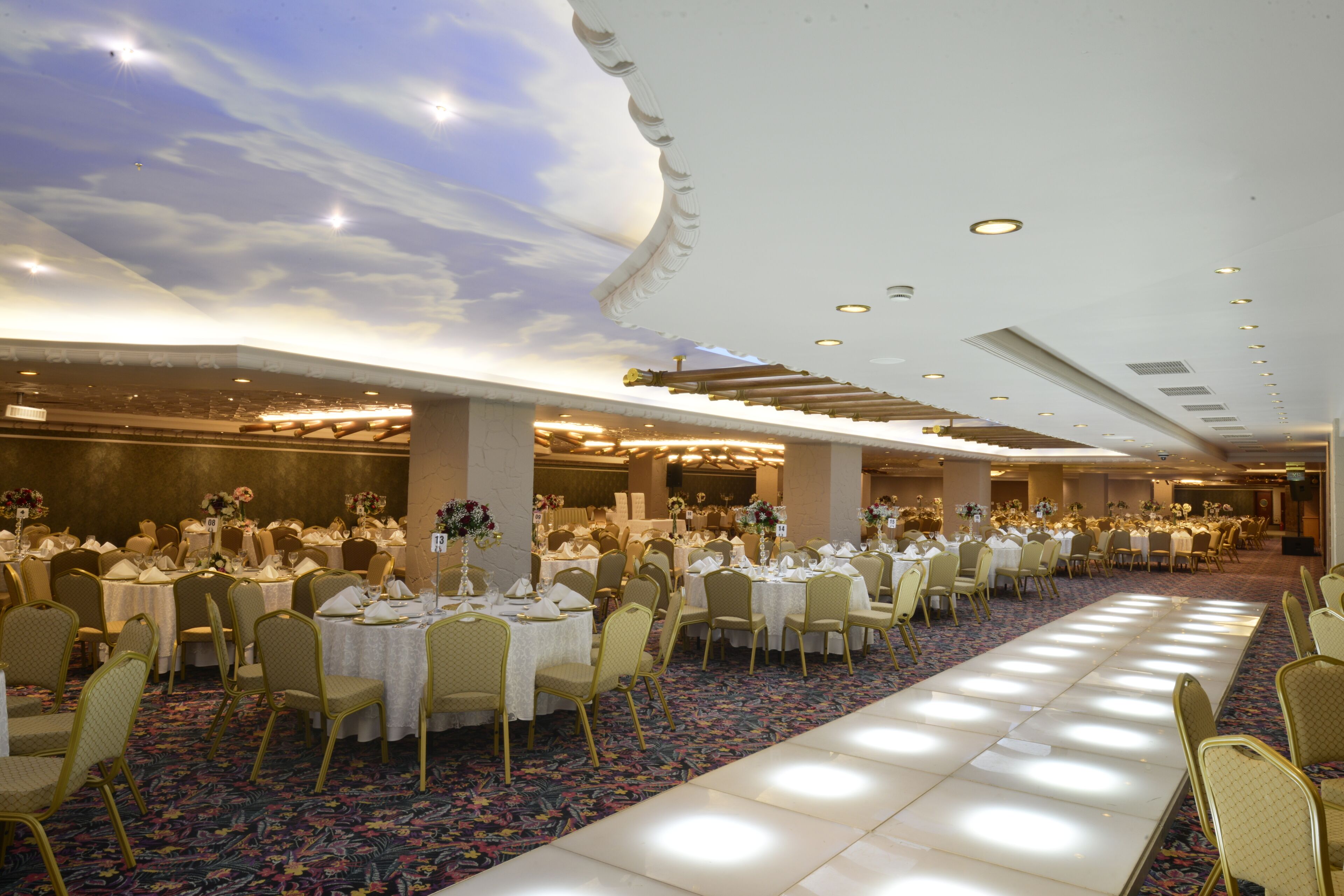Un salón de banquetes con mesas y sillas redondas, una alfombra estampada y un techo decorativo.