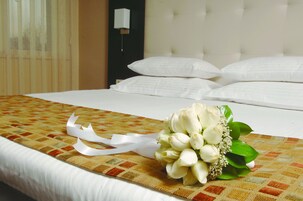 Una habitación de hotel con una cama bien hecha, un ramo de flores blancas y un lazo decorativo en la colcha.