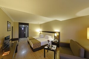 Una habitación de hotel con cama, escritorio, televisor, una mesa lista para comer y un sofá.