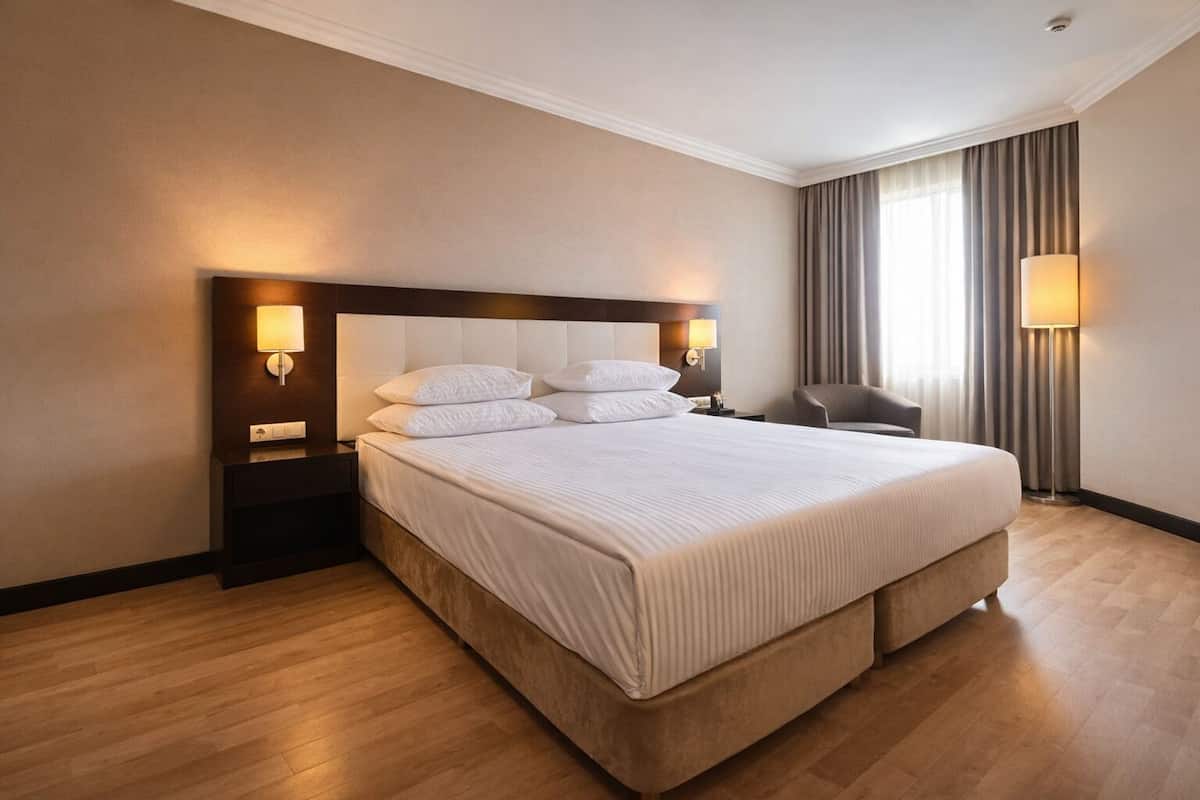 A hotel room with a large bed, two bedside tables with lamps, a chair, and a window with curtains.