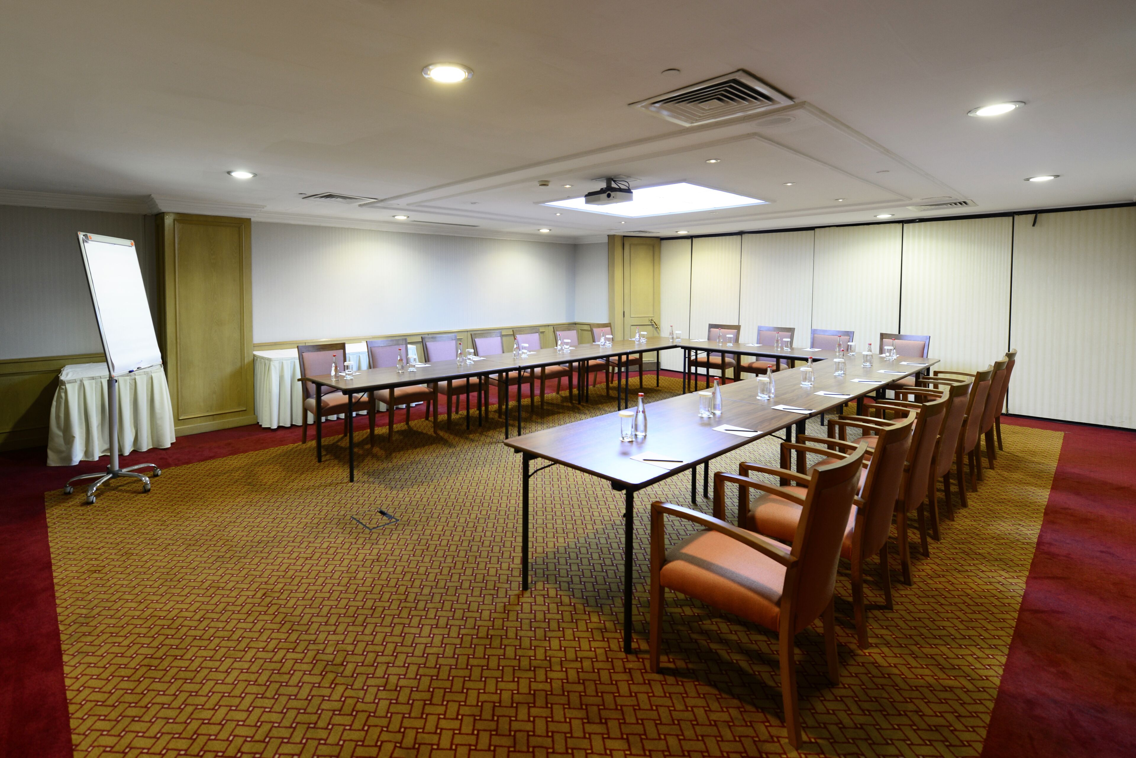 Uma sala de conferências com uma mesa comprida, cadeiras, um quadro branco e um projetor.