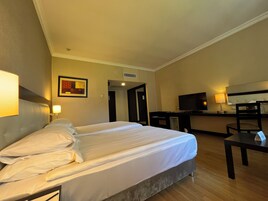 A hotel room with a bed, a desk, a television, and a painting on the wall.