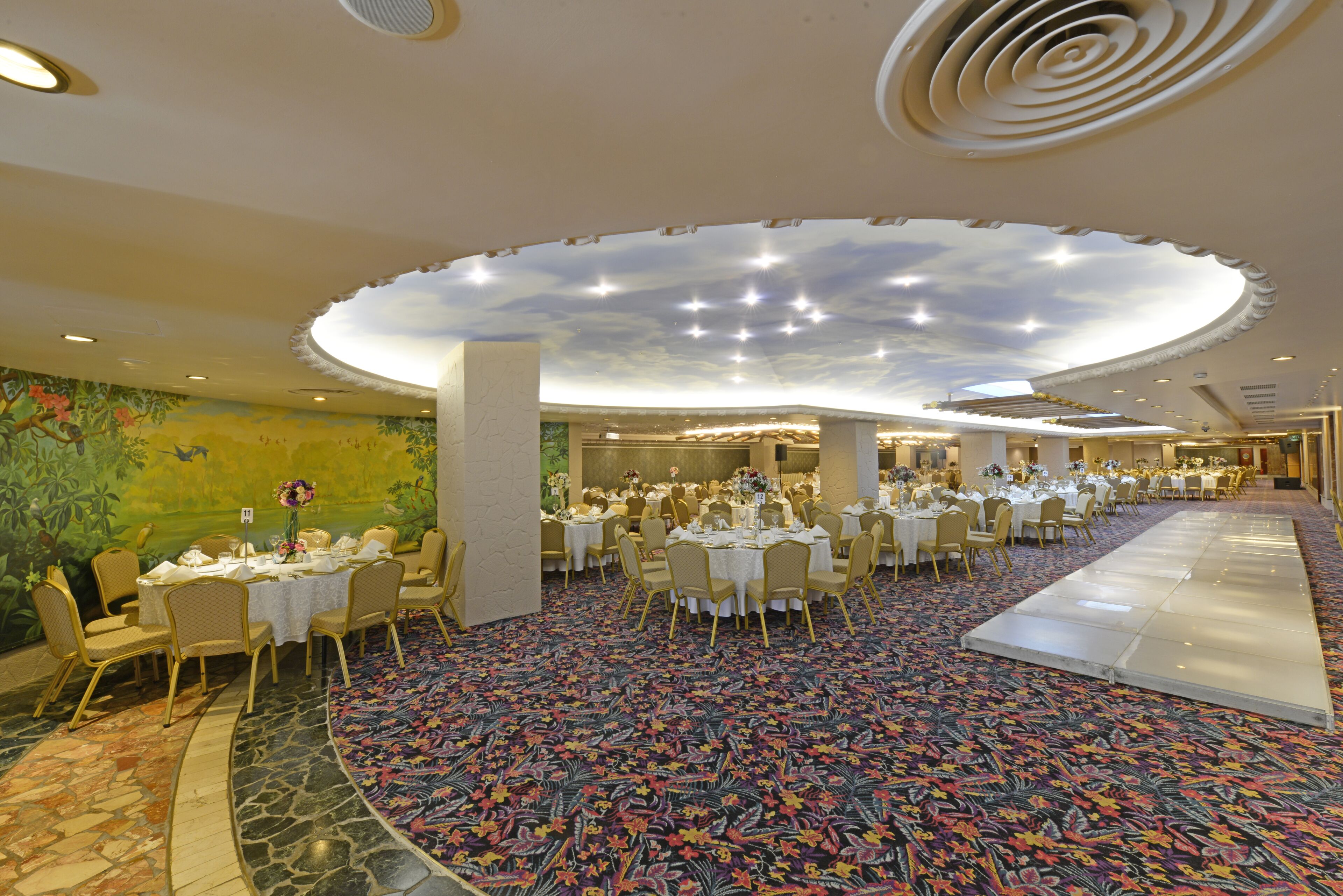 A banquet hall with round tables, chairs, and a ceiling with a starry design.