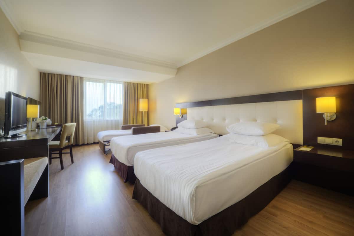 A hotel room with three beds, a desk with a TV, and a chair.