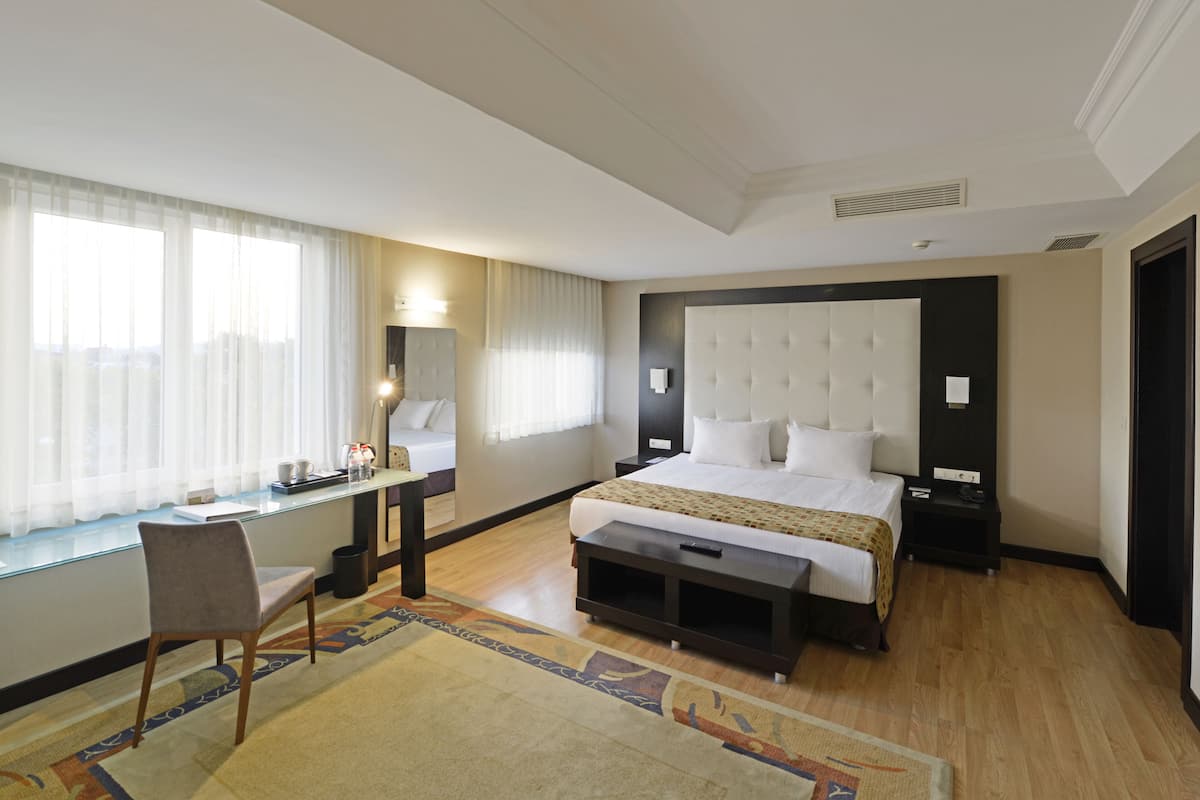 A hotel room with a large bed, a desk, a chair, and a window with curtains.