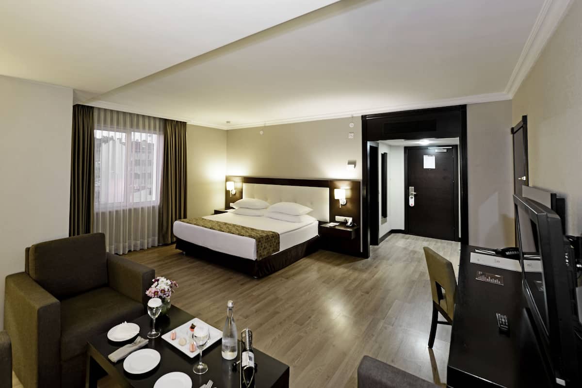 A hotel room with a bed, a desk with a chair, a TV, and a dining area with a table set for two.