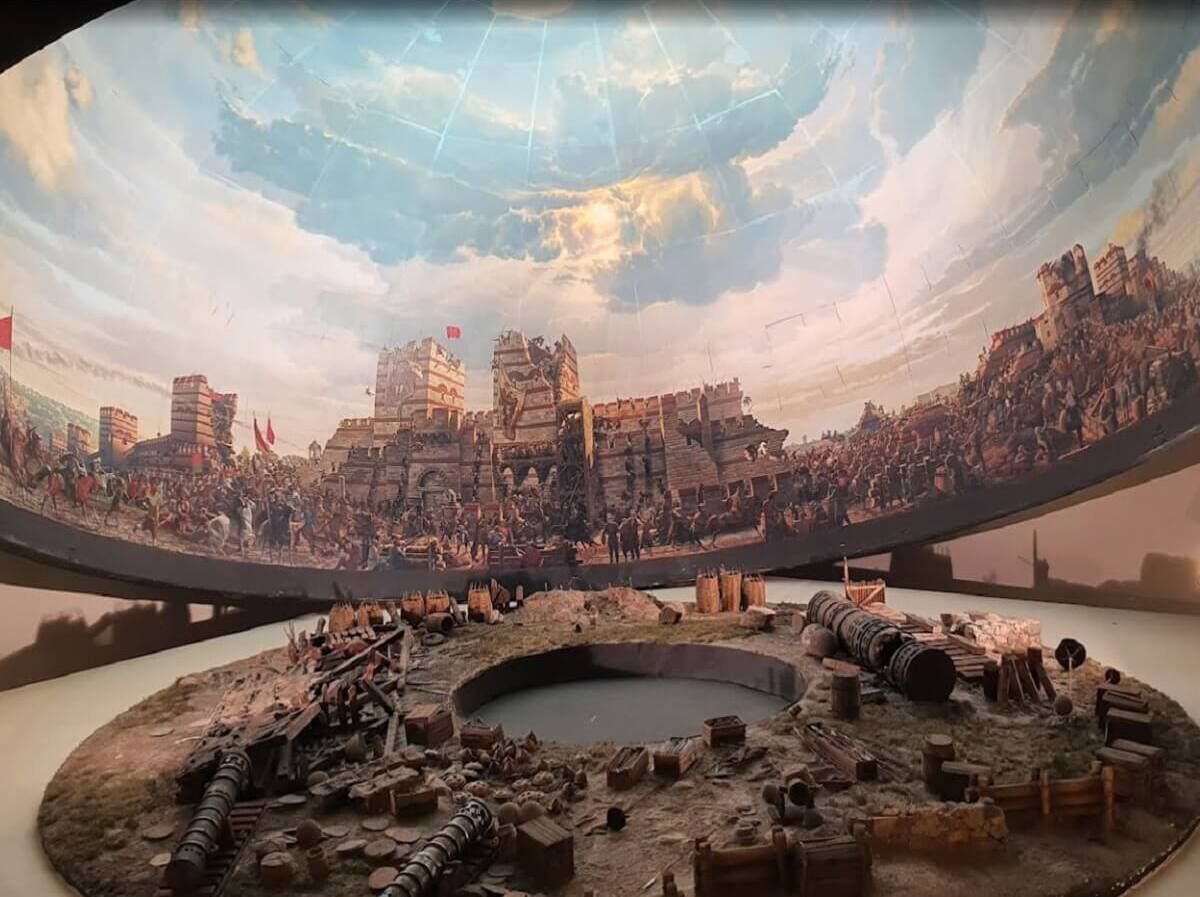 Vista panorámica de una escena de batalla histórica con ruinas circulares en primer plano.