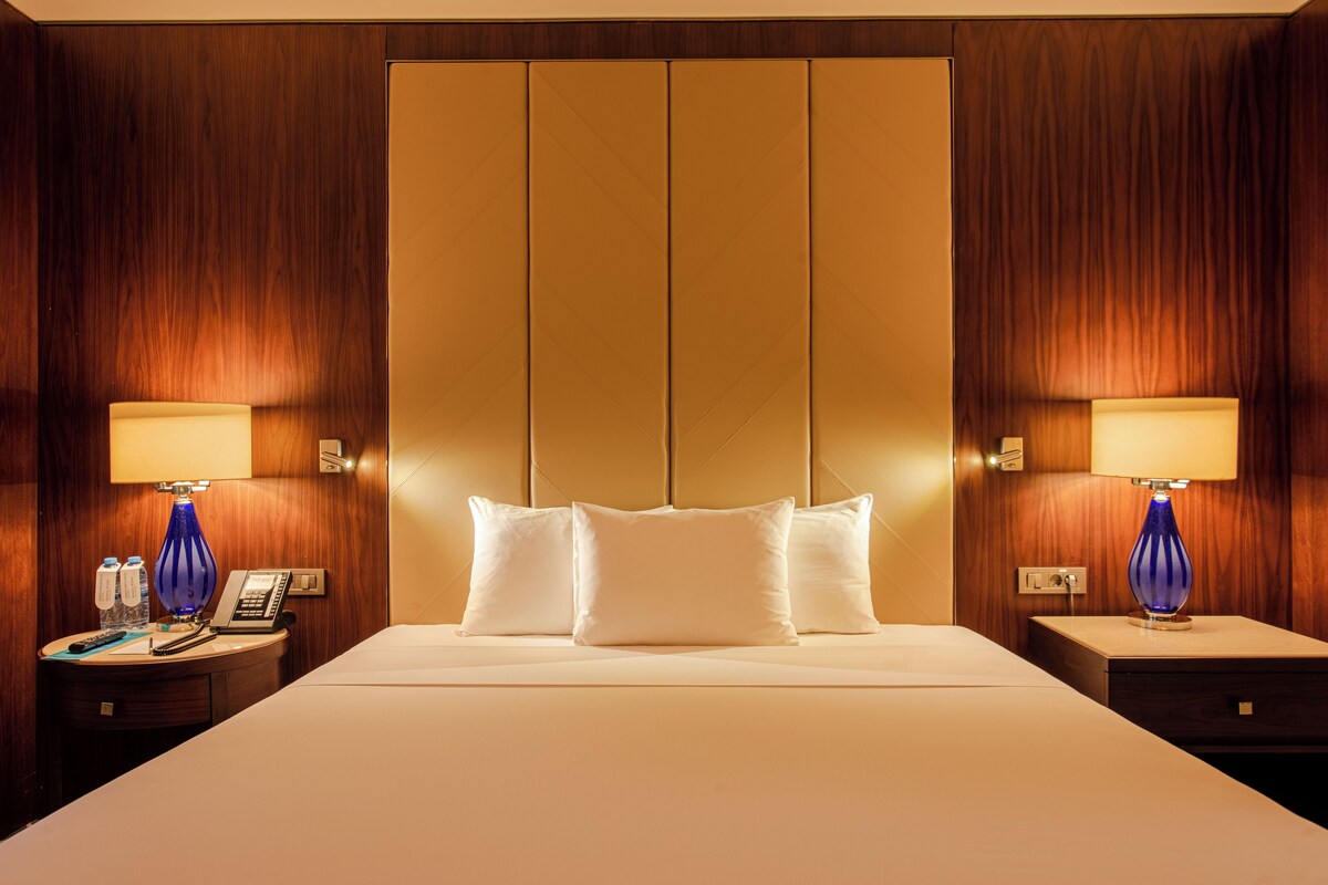Ein Hotelzimmer mit einem großen Bett, zwei Nachttischen, einer Lampe, einem Telefon und einer Wasserflasche.
