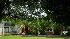 Un jardin luxuriant avec un sentier menant à un bâtiment doté de grandes fenêtres et d’un mur en briques.
