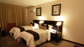 Une chambre d’hôtel avec deux lits, une chaise, un bureau et une lampe.