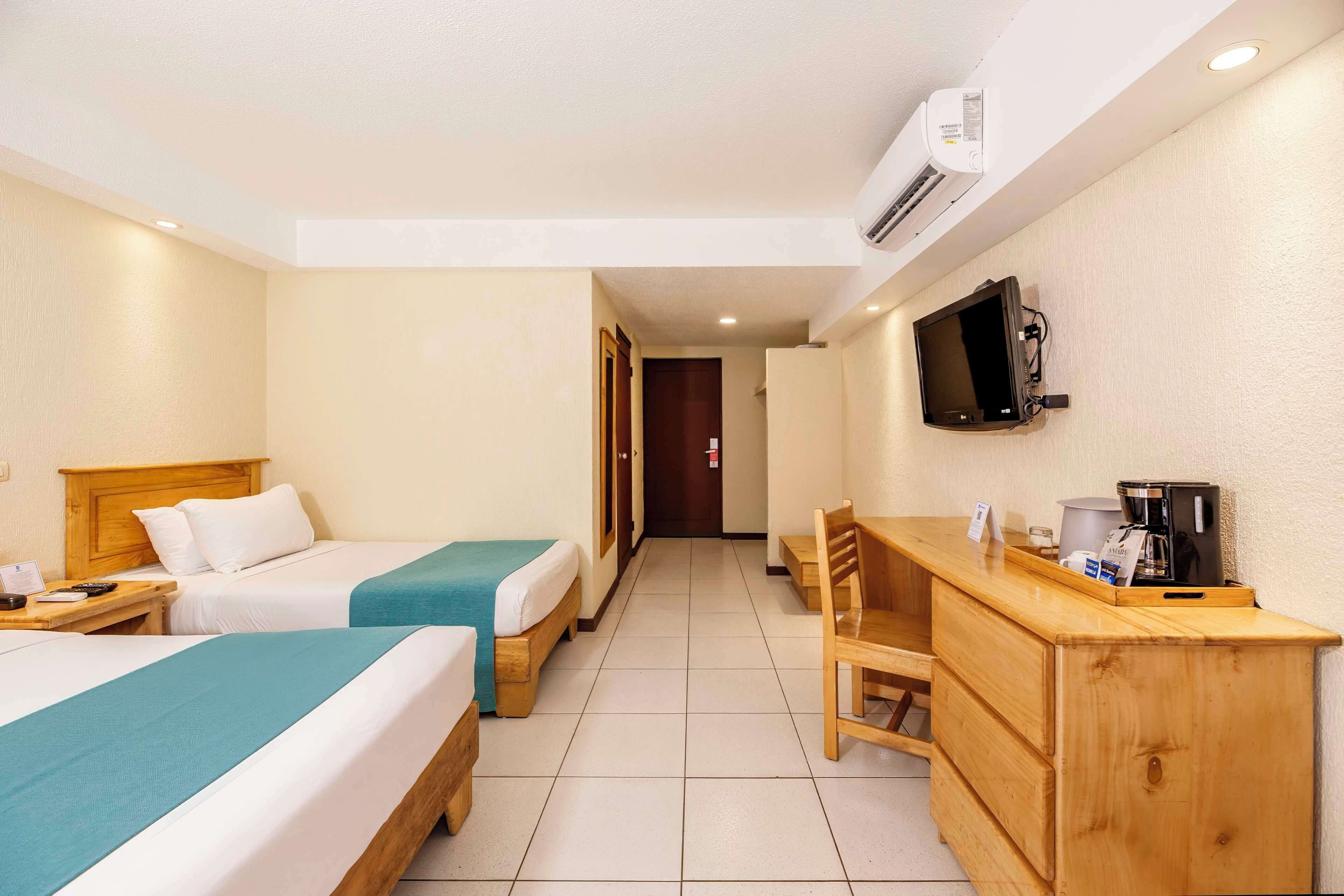 A hotel room with two beds, a desk, a chair, a television, and a coffee machine.