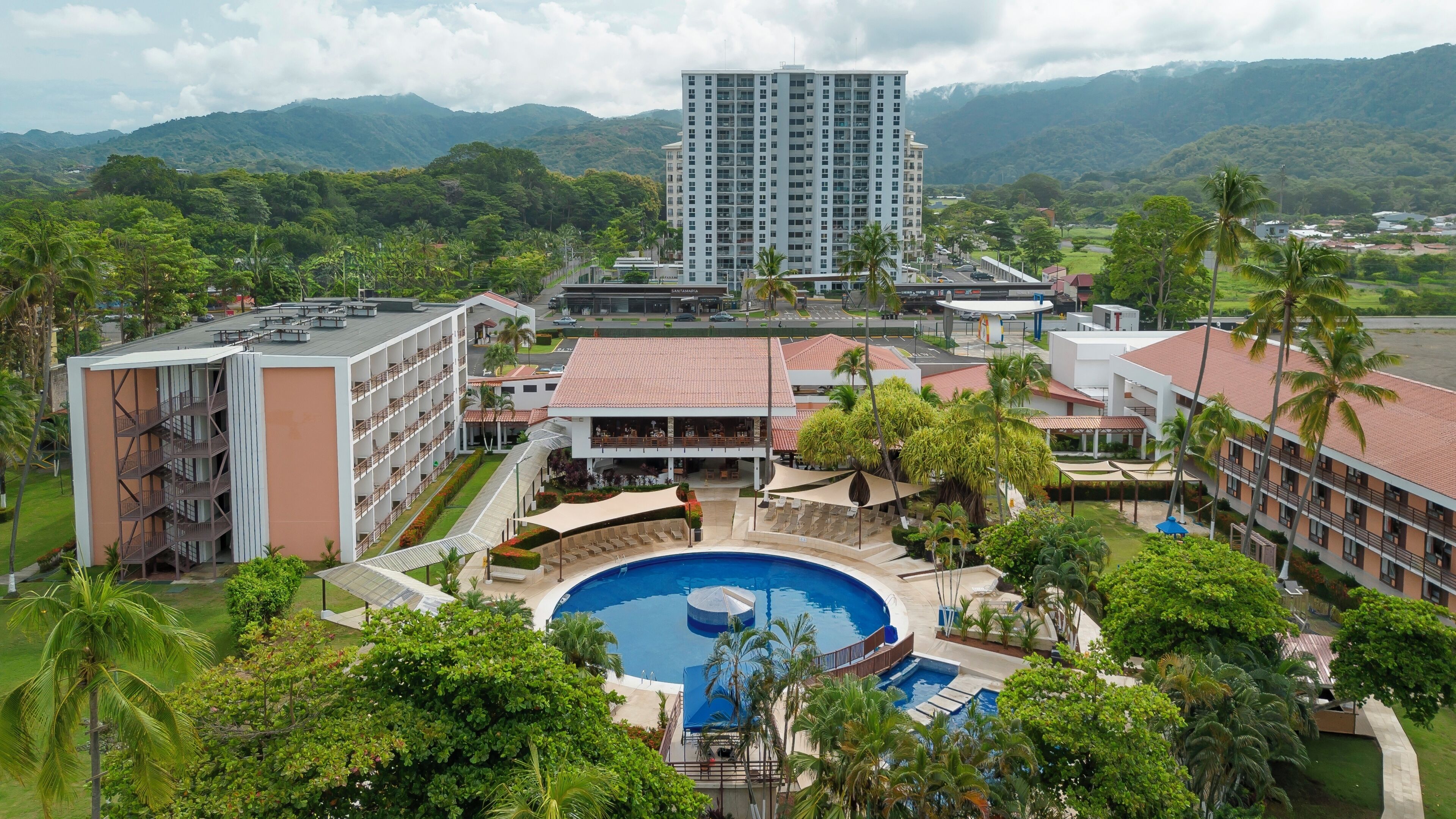 A hotel with a swimming pool, multiple buildings, and a mountainous backdrop.