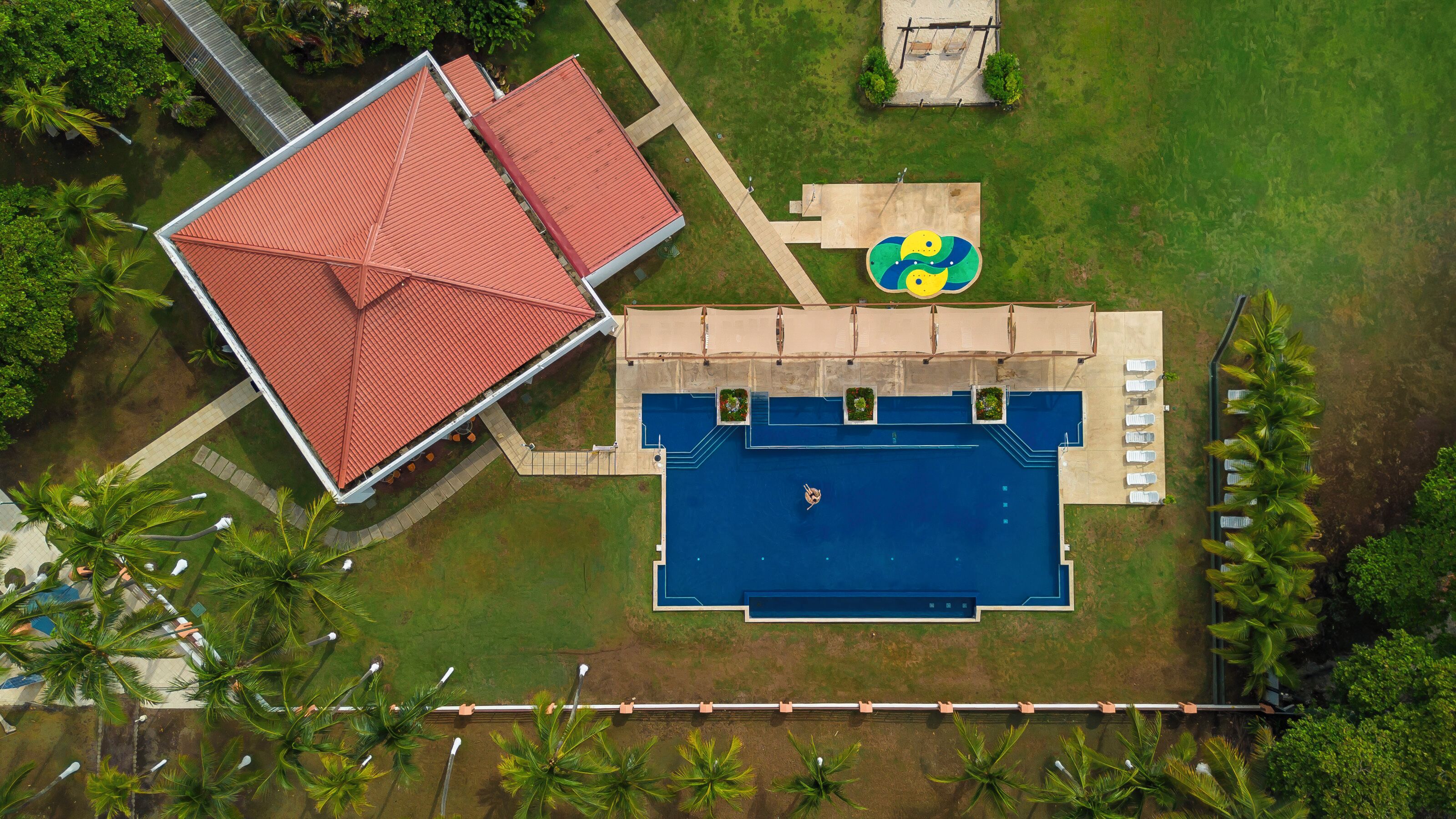 An aerial view of a property with a swimming pool, a covered patio area, and a red-roofed building.