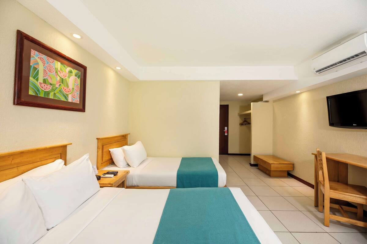 A hotel room with two beds, a TV, and a desk.