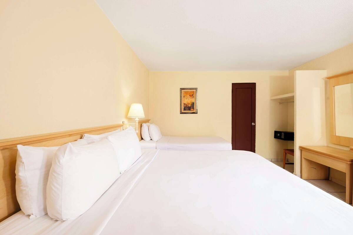 A hotel room with two beds, a desk, a chair, a lamp, a door, and a painting on the wall.