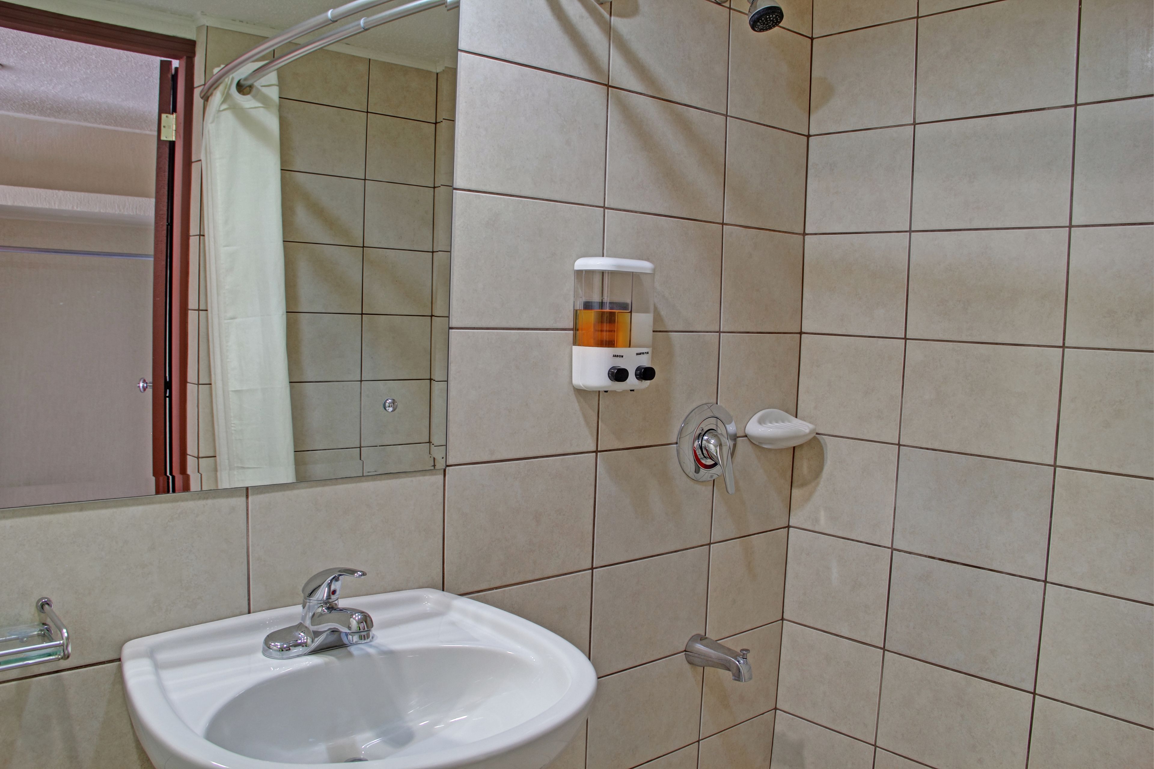 A bathroom with a sink, mirror, and a soap dispenser on the wall.