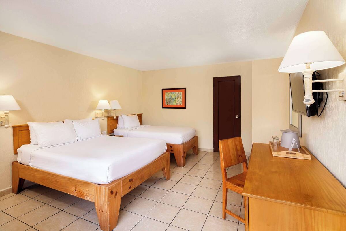 A hotel room with two wooden beds, a wooden desk, and a chair.