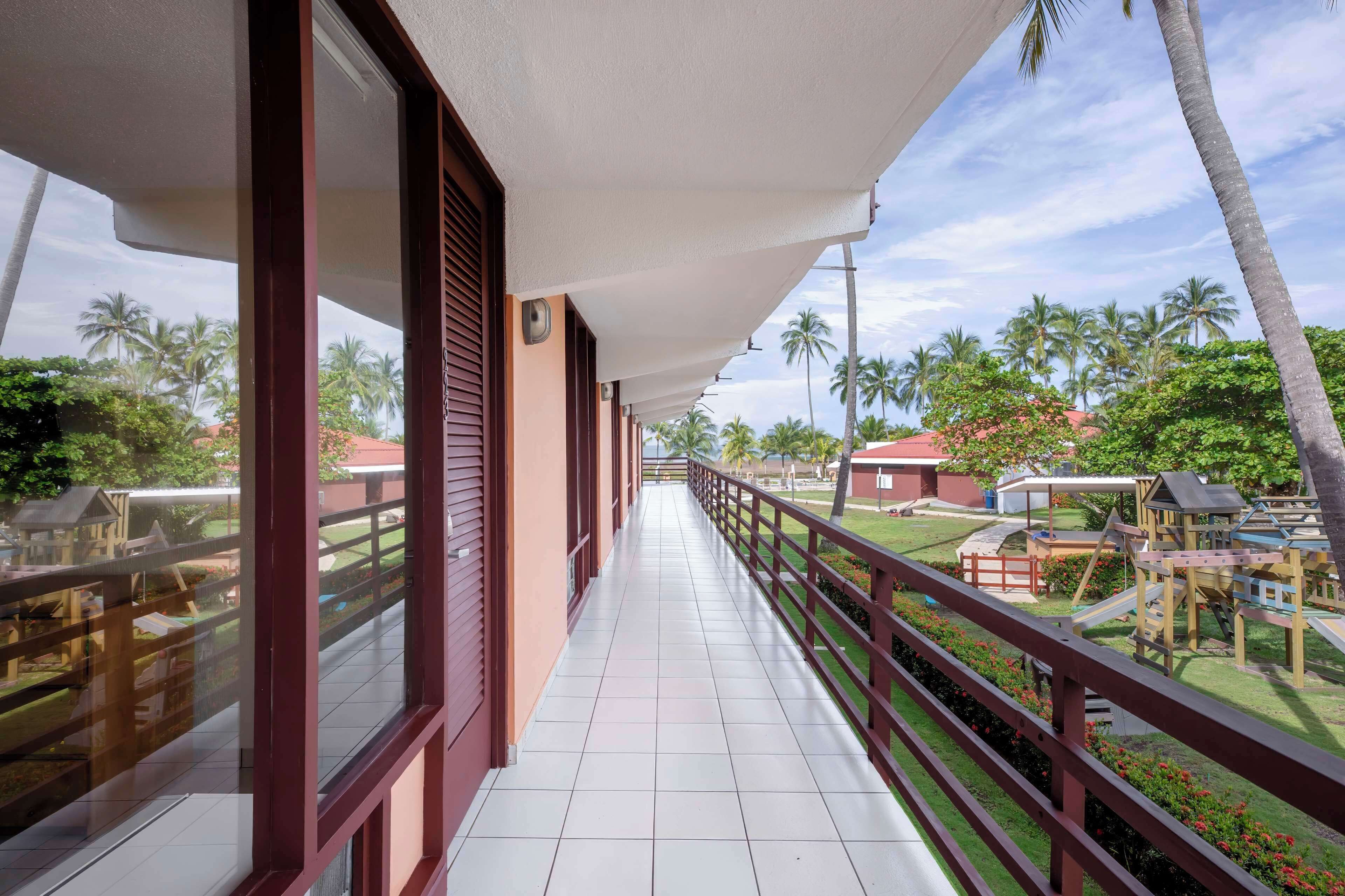 A covered balcony with a view of a playground and palm trees.