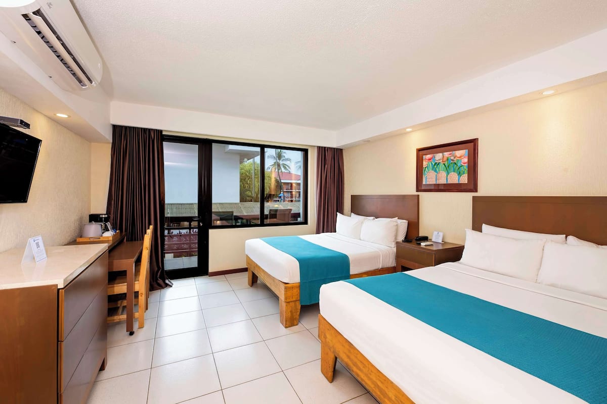 A hotel room with two beds, a desk, a chair, a TV, and a window with curtains.