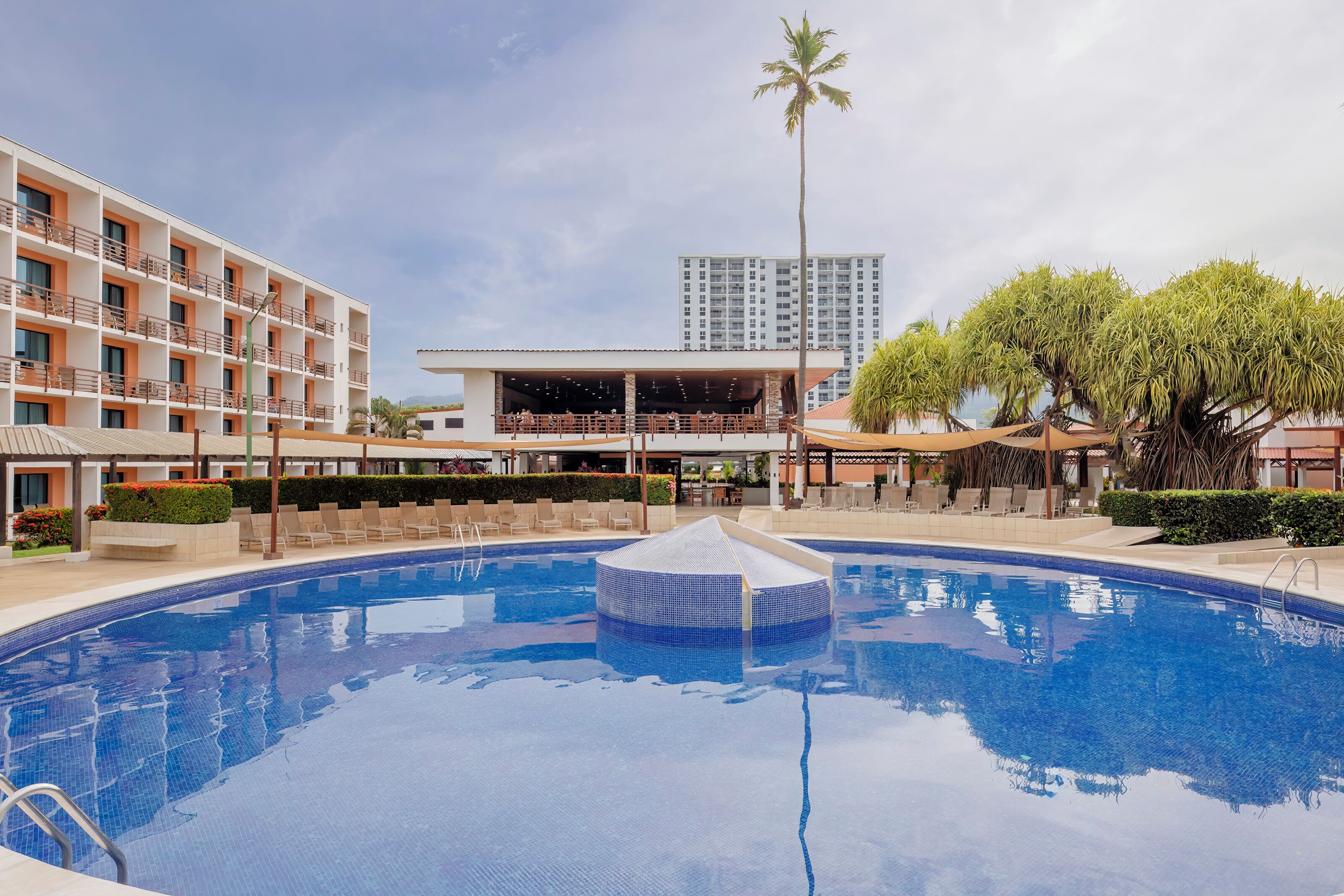 A hotel with a swimming pool, outdoor seating, and a tall building in the background.