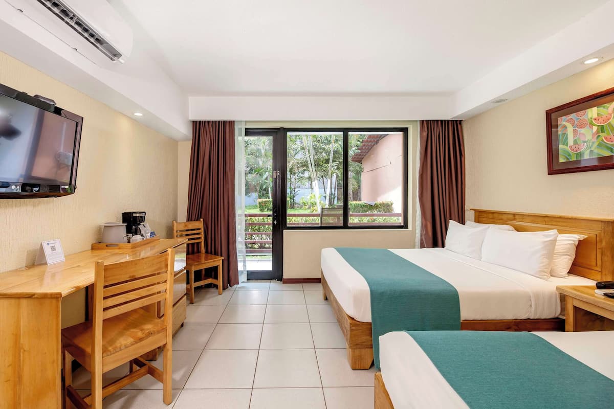A hotel room with a bed, a desk, a chair, a TV, and a window with curtains.