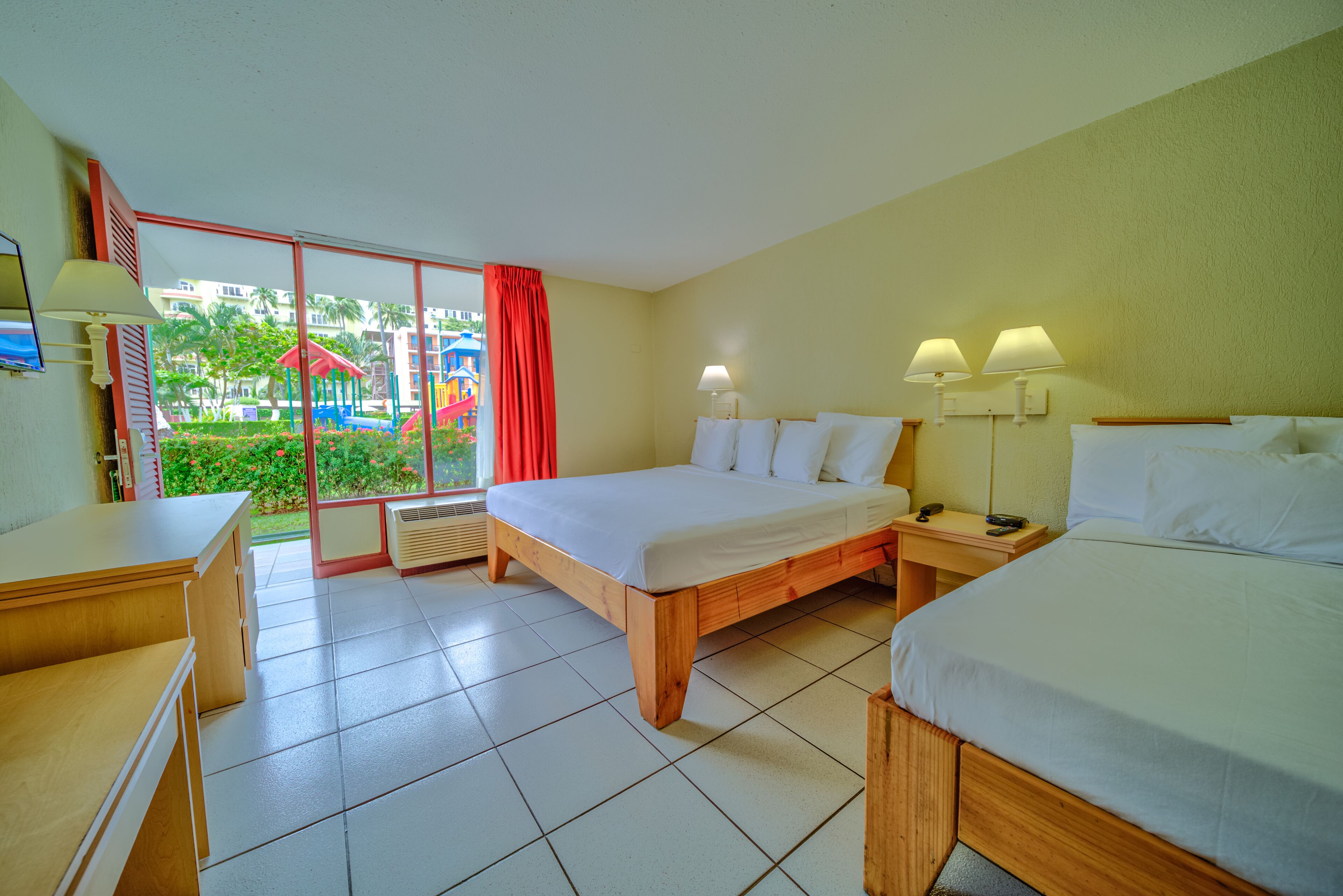 Une chambre d’hôtel avec un grand lit, un bureau et une vue sur un terrain de jeux, accessible par une porte coulissante.