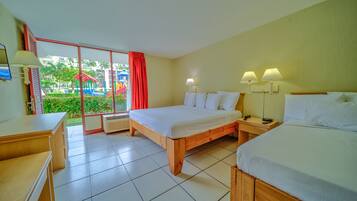 A hotel room with a large bed, a desk, and a view of a playground through a sliding door.
