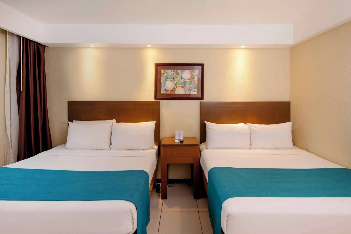 A hotel room with two beds, a nightstand, and a framed picture on the wall.