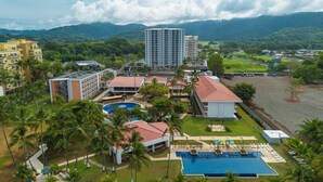 A resort with multiple swimming pools, a large building, and a mountainous backdrop.