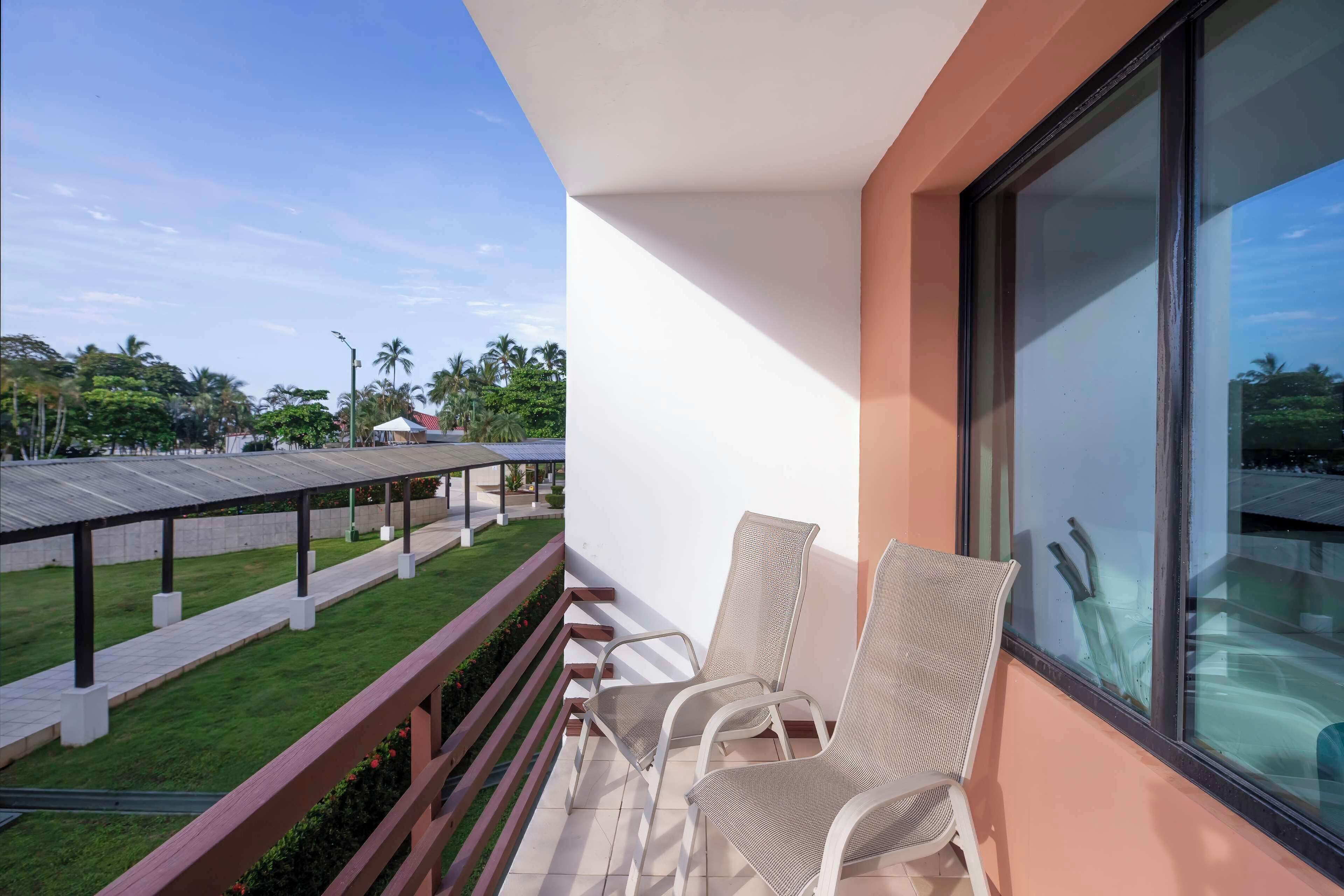 A balcony with two chairs and a view of a covered outdoor area with a pool.