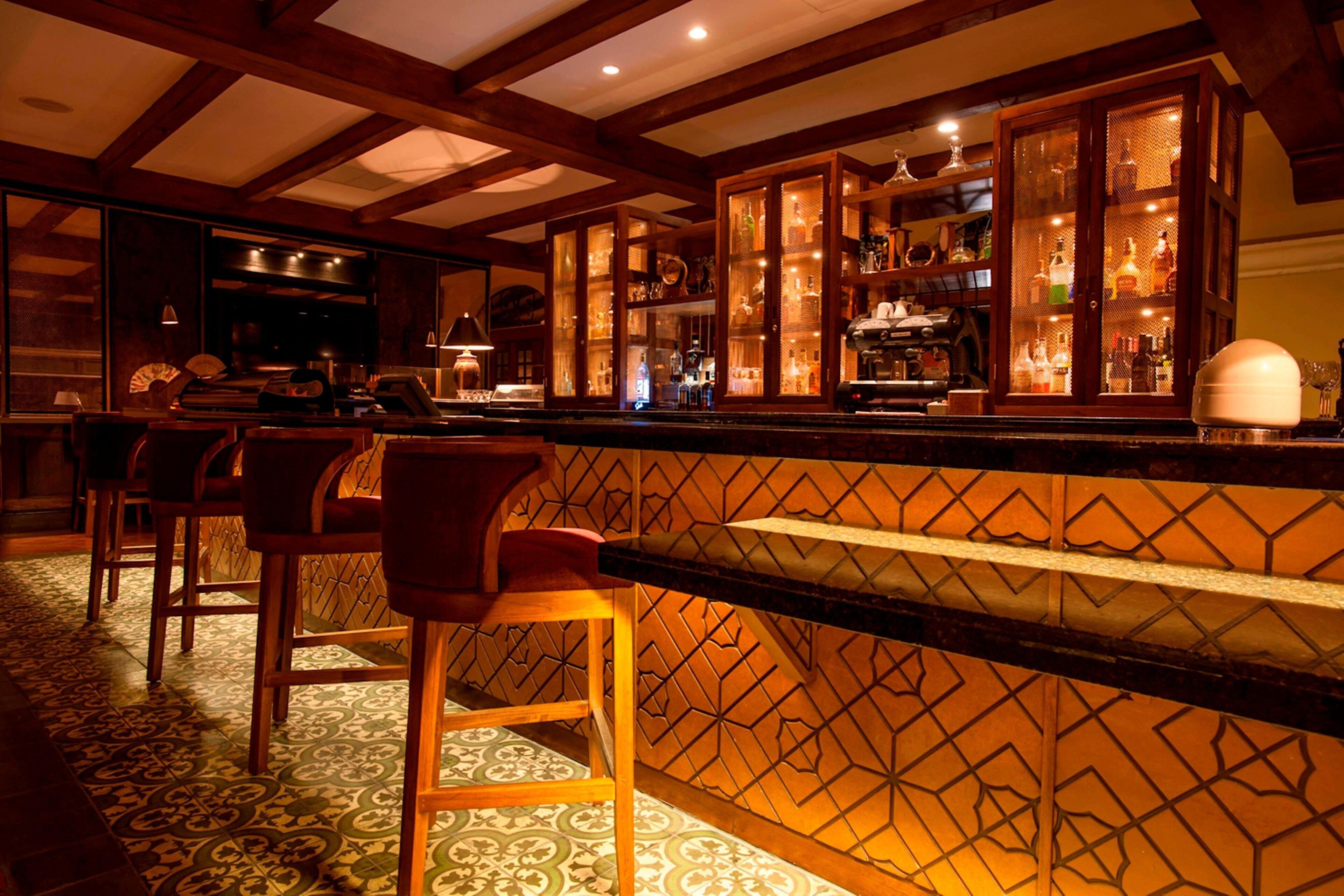 A bar area with wooden chairs, a patterned floor, and a bar counter with a decorative back panel.