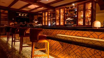 A bar area with wooden chairs, a patterned floor, and a bar counter with a decorative back panel.