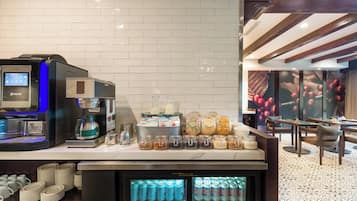 Uma estação de café com uma máquina de café KREa, um dispensador de bebidas e um refrigerador para bebidas.