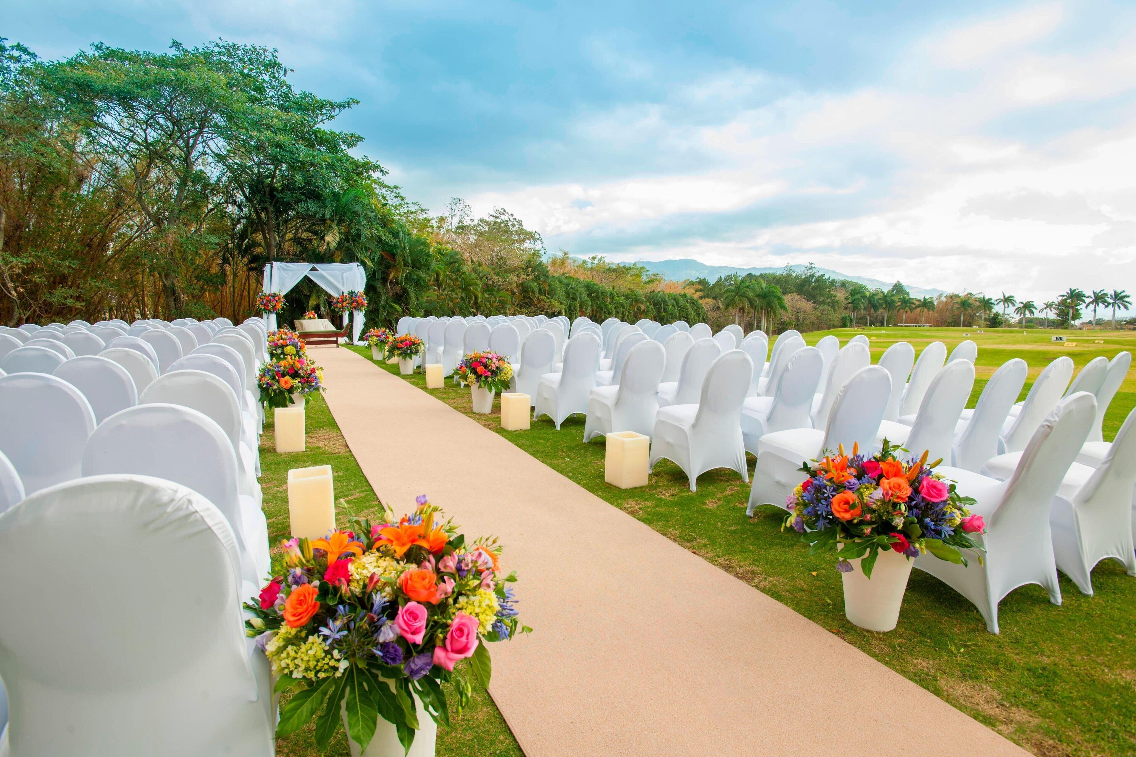 A wedding aisle with white chairs and floral arrangements.