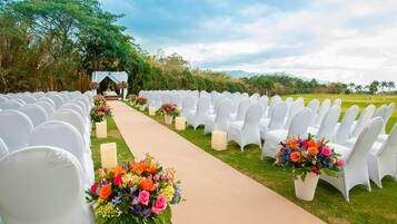 A wedding aisle with white chairs and floral arrangements.