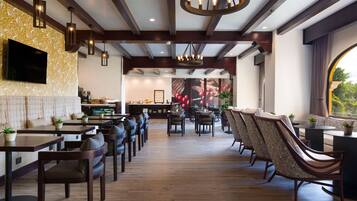 Un ristorante con pavimento in legno, sedie scure e tavoli. È presente una televisione montata a parete e un lampadario appeso al soffitto.
