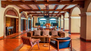 Un hall amplio con suelo de madera, un área de estar central con sofás y sillones, y puertas arqueadas que dan a otras salas.