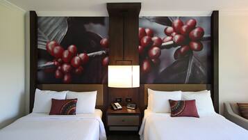 Habitación de hotel con dos camas, una mesita de noche con teléfono y lámpara, y un gran mural con motivos de frutas.