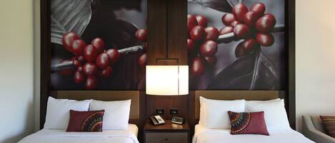 Une chambre d’hôtel avec deux lits, une table de chevet avec un téléphone et une lampe, et une grande fresque murale sur le thème des fruits.