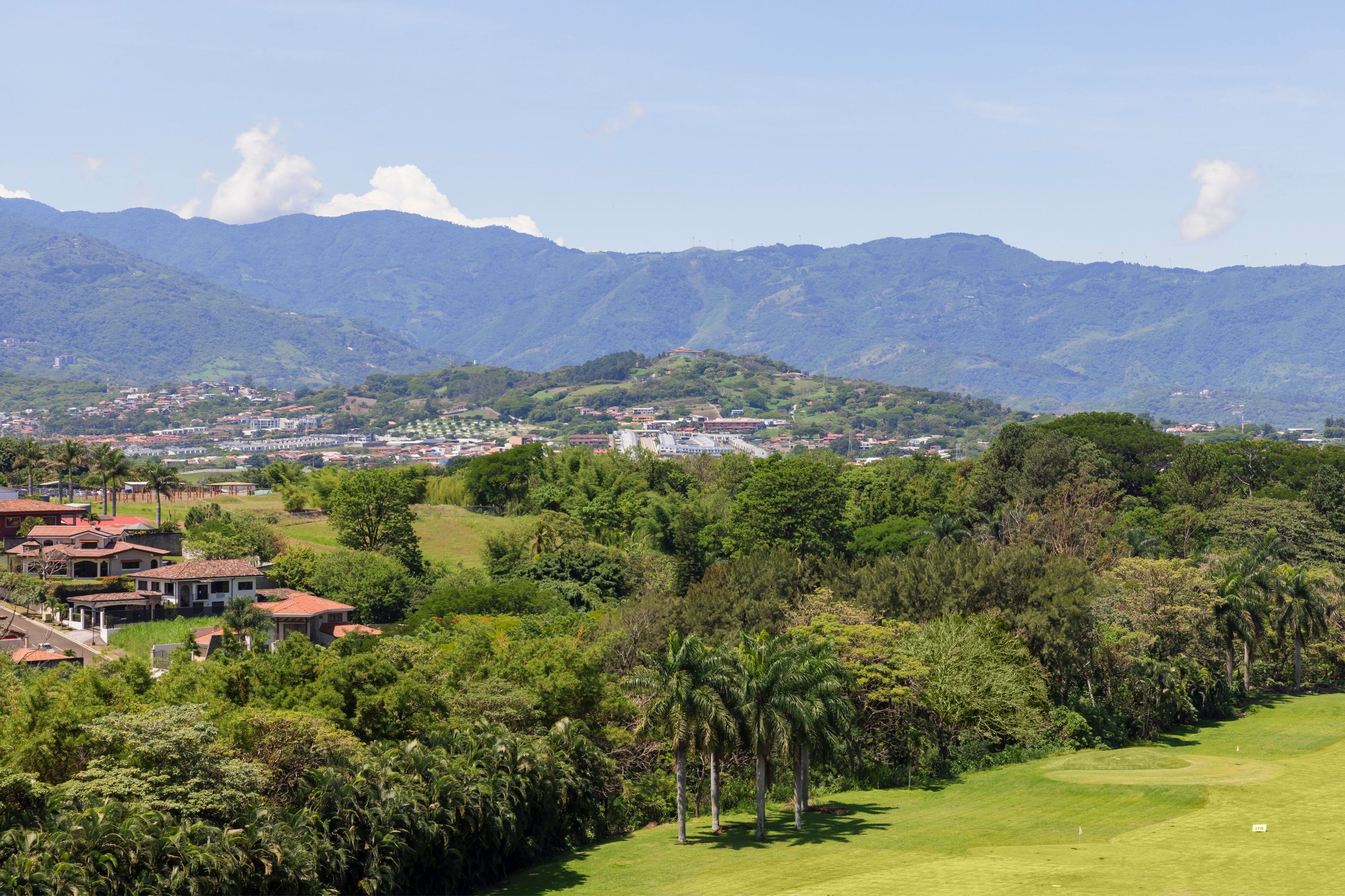 A residential area with houses, a golf course, and mountains in the background.