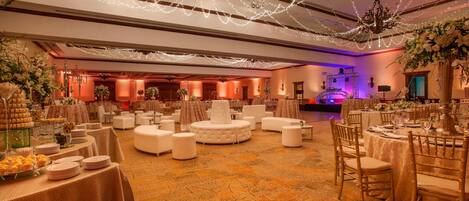 A banquet hall with round tables, white chairs, and a carpeted floor.
