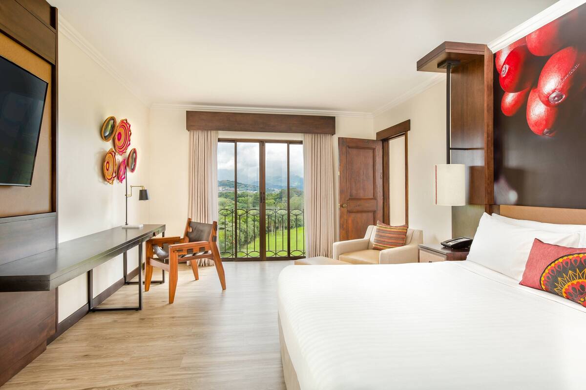 Ein Hotelzimmer mit Bett, Schreibtisch, Stuhl, Fernseher und Blick ins Freie.